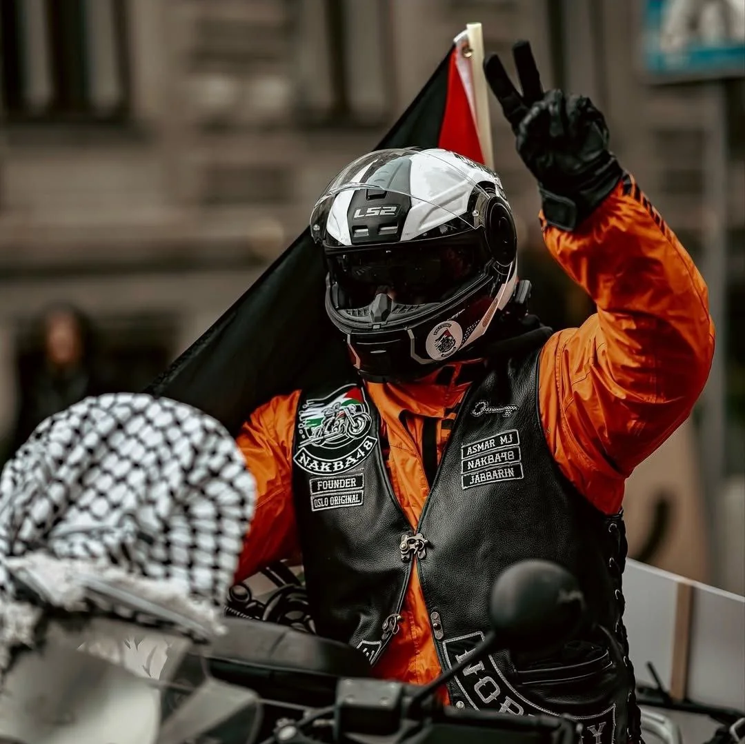 Motorist v oranžni jakni z dvignjeno roko in palestinsko zastavo.
